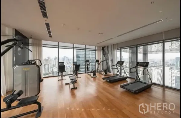 Condominium for rent or sale in Watthana, Bangkok - High-floor fitness center with treadmills and gym machines facing the skyline.