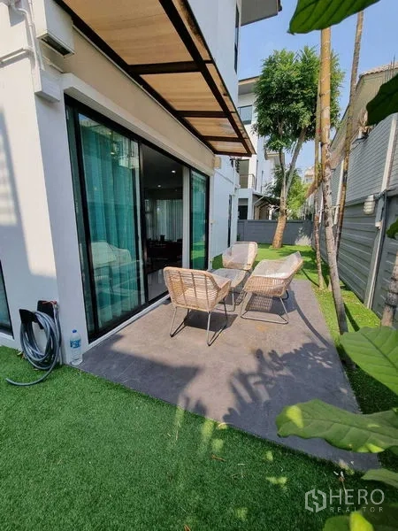 Detached House for rent or sale in Prawet, Bangkok - Side patio with outdoor table and chairs on artificial grass beside sliding doors.