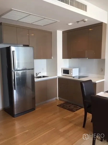 Condominium for rent in Khlong Toei, Bangkok - Compact L-shaped kitchen with high-gloss cabinets, sink, cooktop space, microwave and full-size refrigerator.