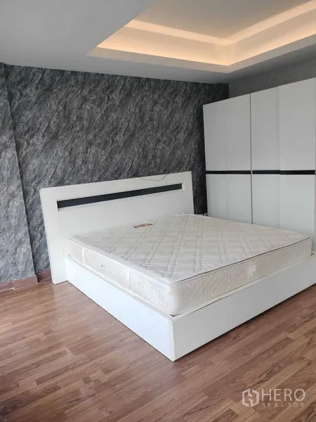 Townhouse for rent in Bueng Kum, Bangkok - Bedroom with white platform bed, wardrobe, wood floors and a stone-texture accent wall.