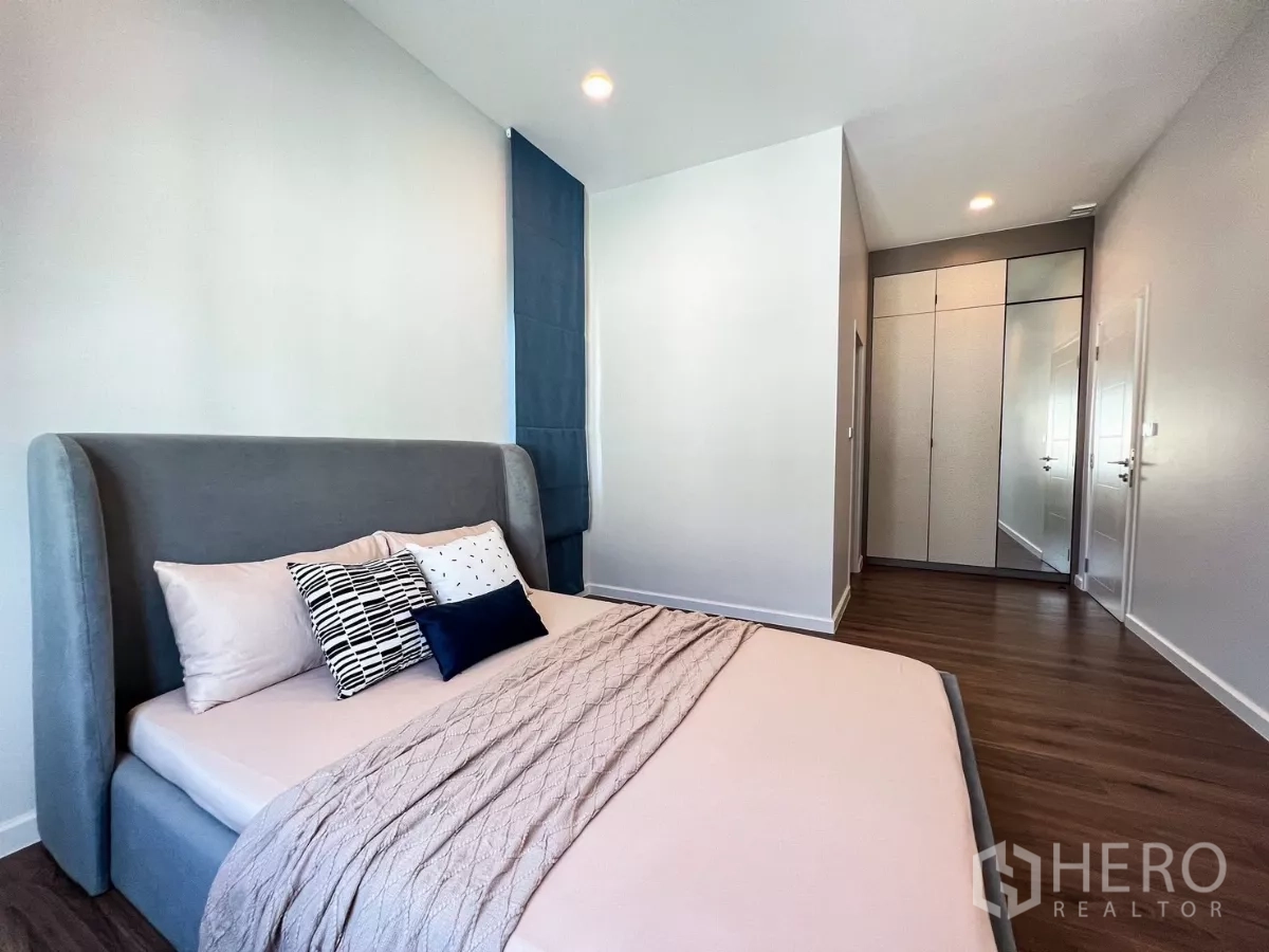 Detached House for rent in Khan Na Yao, Bangkok - Cozy bedroom with gray upholstered bed, wood flooring and built-in wardrobes.