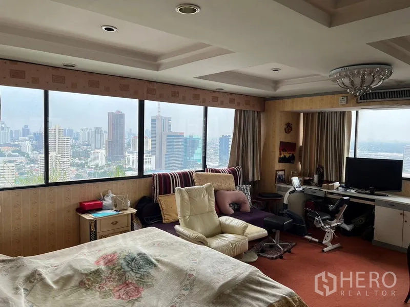 Condominium for sale in Khlong Toei, Bangkok - Master bedroom with panoramic windows, Bangkok skyline views, lounge chairs and a work desk.
