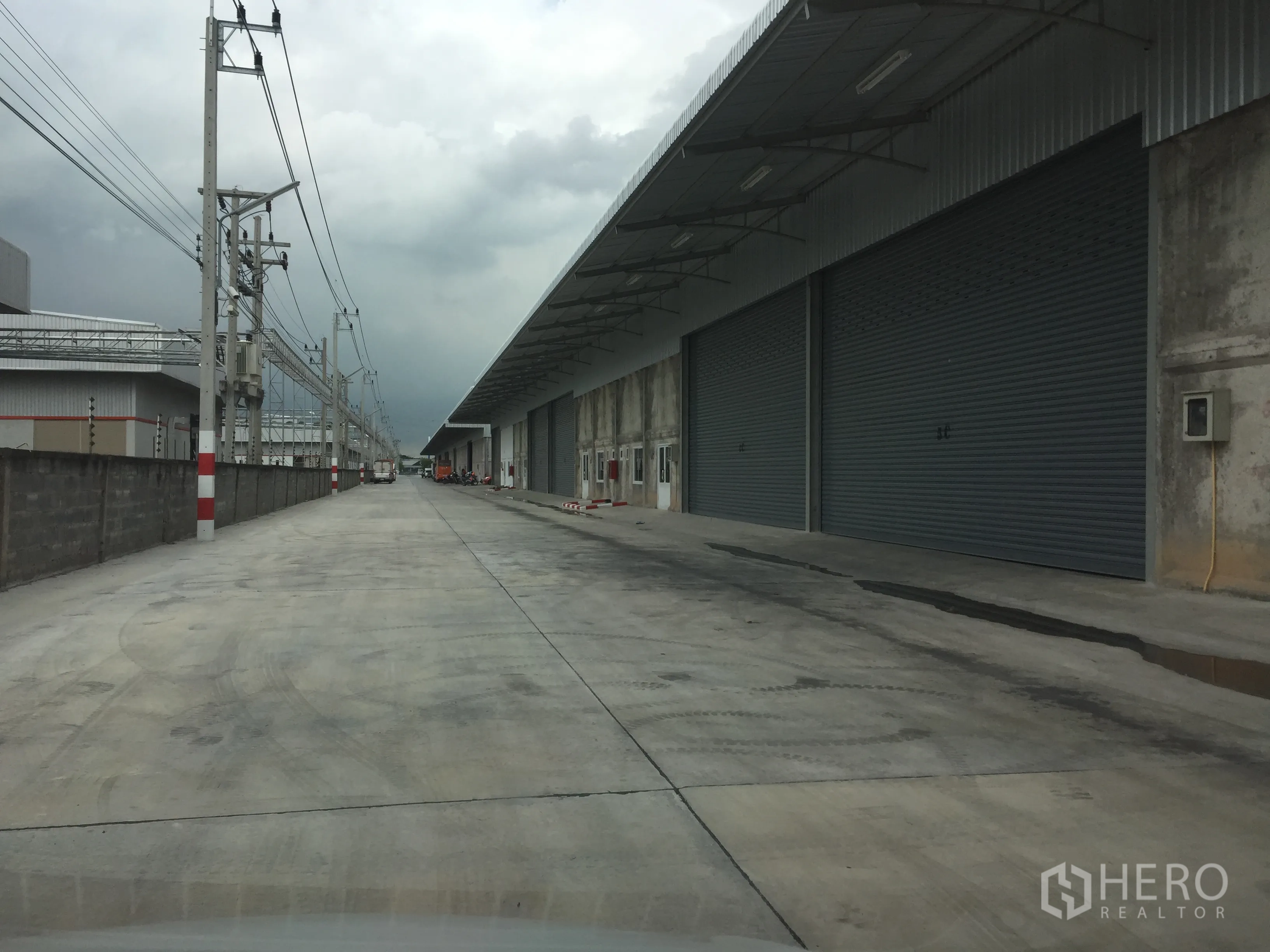 Warehouse for rent in Lam Luk Ka, Pathum Thani - External drive lane with long canopy and multiple large roller doors for truck access.