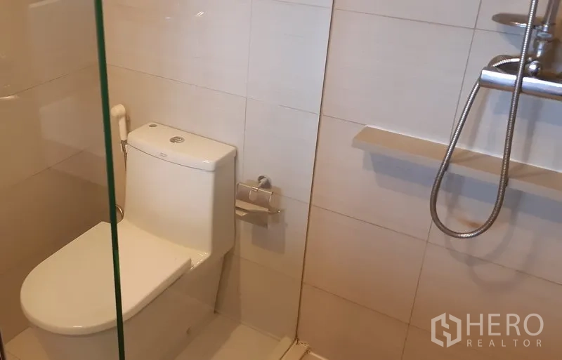 Condominium for rent in Khlong Toei, Bangkok - Clean bathroom with glass-enclosed shower, handheld showerhead and modern toilet.