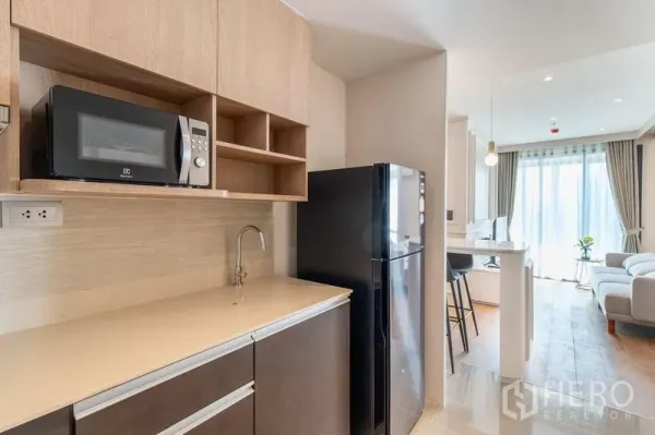 Condominium for rent in Ratchathewi, Bangkok - Compact pantry kitchen with built-in cabinets, microwave, fridge and sink leading to the living area.
