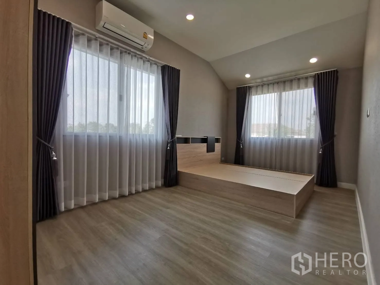 บ้านเดี่ยว for rent in Bang Phli, Samut Prakan - ห้องนอนหลักพร้อมเตียงยกพื้น ไฟดาวน์ไลท์ หน้าต่างสองบาน ผ้าม่าน และเครื่องปรับอากาศ