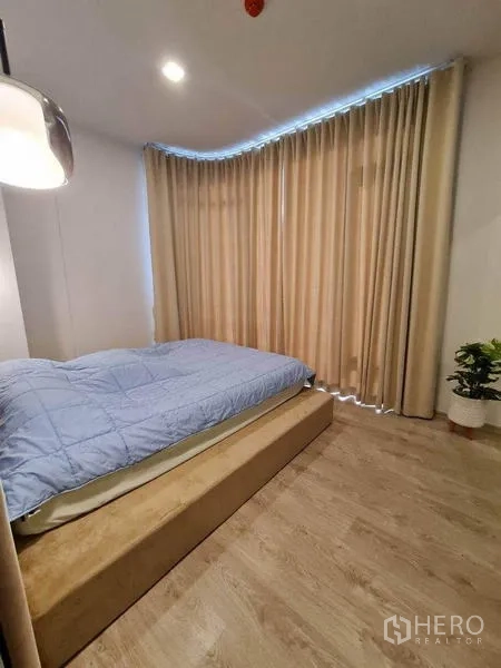 Condominium for rent - Bedroom corner with long beige curtains, platform bed and a potted plant.