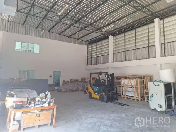 货栈 出售在Pathum Thani - 仓库内部空间开阔，钢结构高顶，通风百叶，旁有叉车与货架。