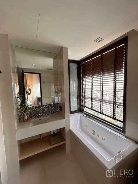 Condominium for rent or sale in Khlong Toei, Bangkok - Bathroom with window-side bathtub, mosaic-tiled vanity and city outlook.