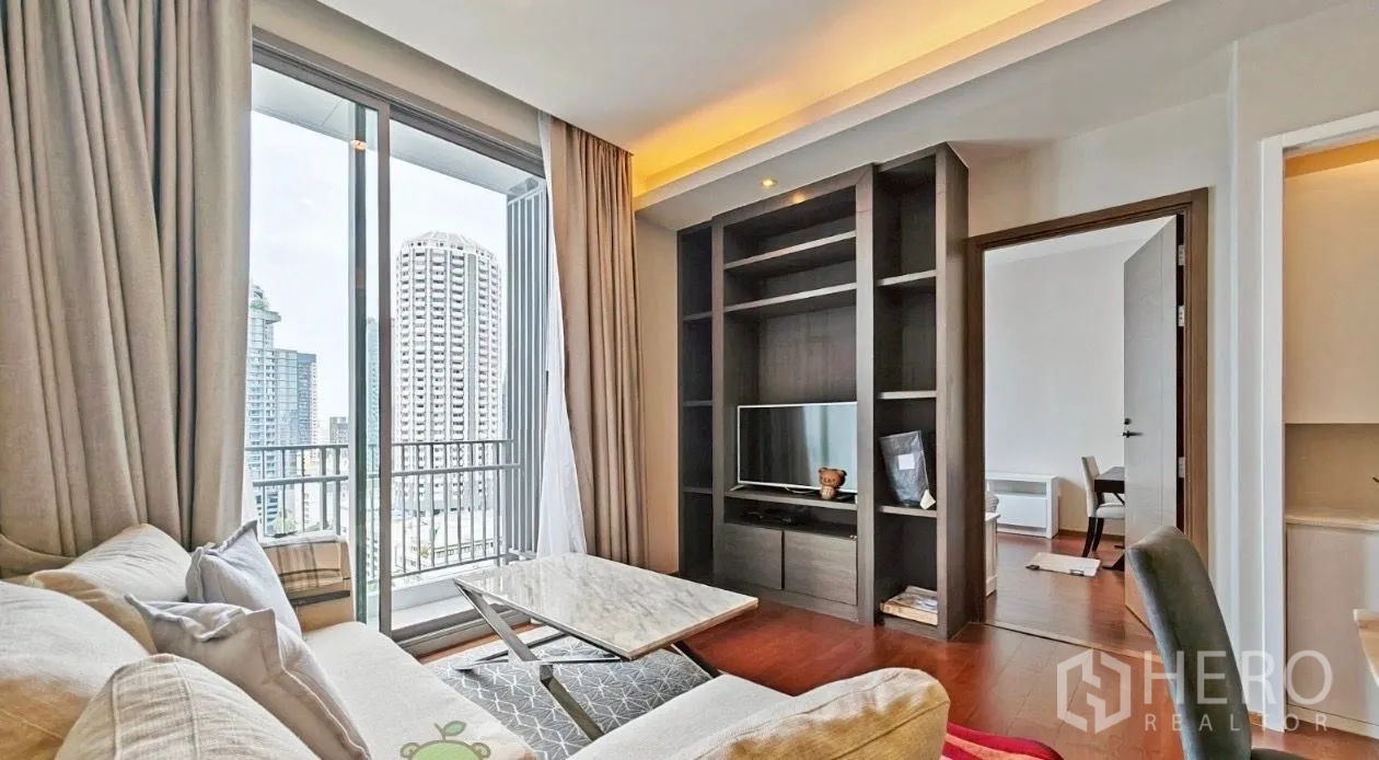 公寓 出租在Watthana, Bangkok - 客厅面向内置书架与电视，旁有阳台及通往卧室的门。