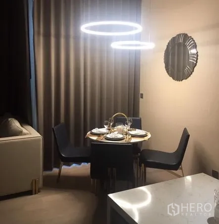 Condominium for rent in Watthana, Bangkok - Cozy dining corner with round table, navy chairs and modern ring pendant lights with curtains drawn.
