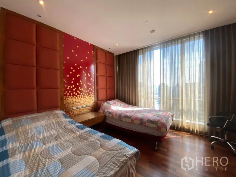 Condominium for rent in Sathon, Bangkok - Twin bedroom with red padded feature wall, wood floors and full-height windows.