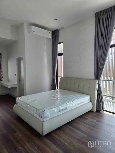 Detached House for rent in Bang Phli, Samut Prakan - Bedroom with upholstered bed, tall windows and gray curtains.