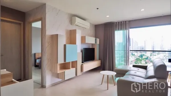 Condominium for rent in Khlong Toei, Bangkok - Bright living room with built-in TV wall, sofa, balcony and Bangkok skyline view.