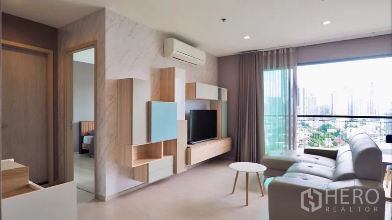 Condominium for rent in Khlong Toei, Bangkok - Bright living room with built-in TV wall, sofa, balcony and Bangkok skyline view.
