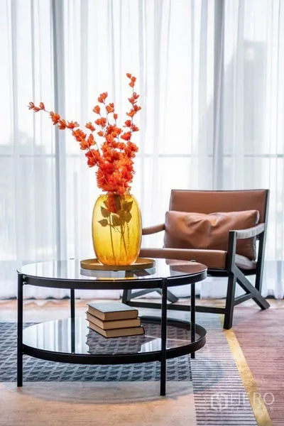 Condominium for rent in Khlong Toei, Bangkok - Glass coffee table with an amber vase and accent chair beside sheer floor-to-ceiling windows.