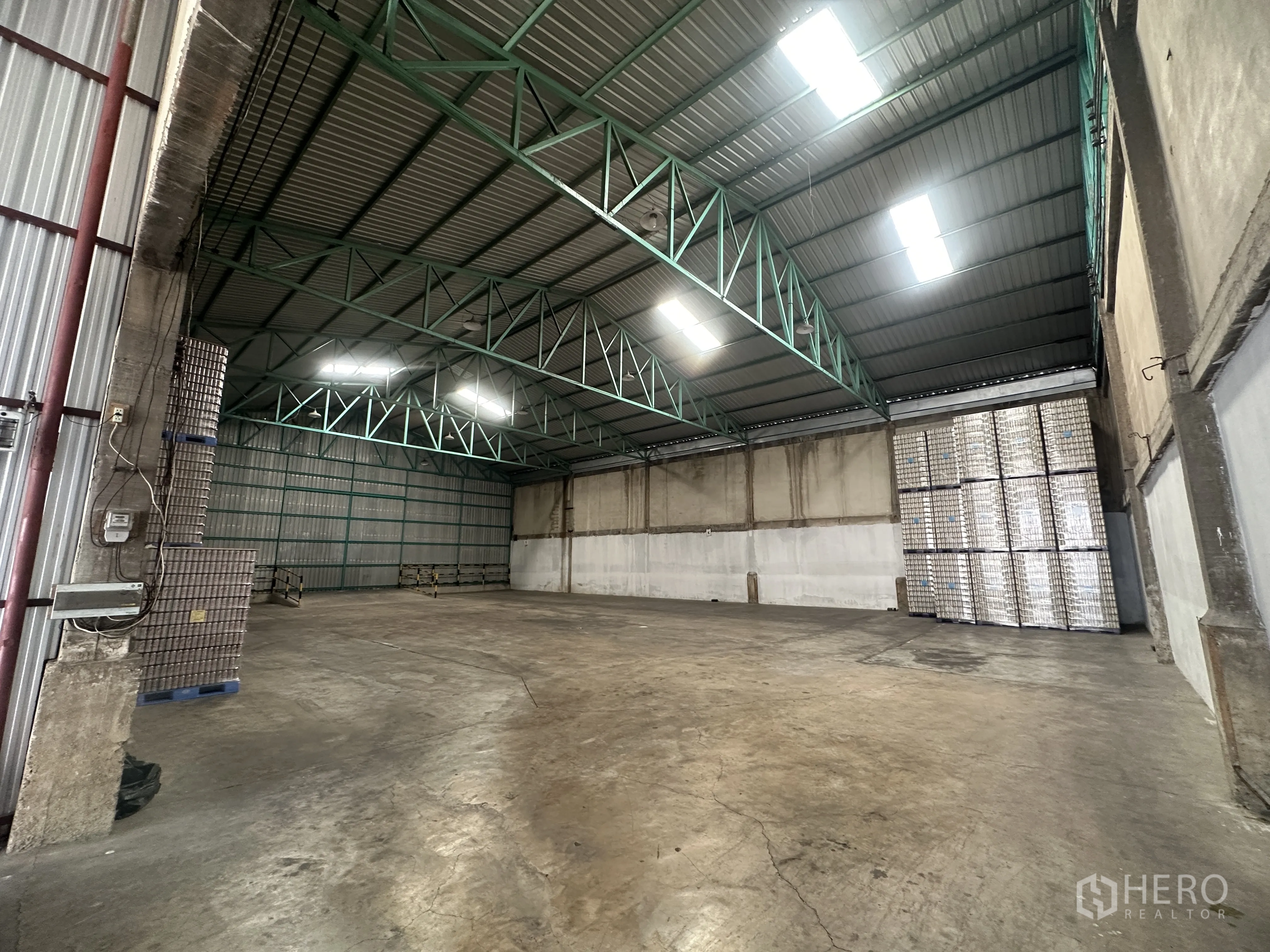 Warehouse for rent in Mueang Pathum Thani, Pathum Thani - Interior angle showing a column-free span, bright roof panels, and stacked pallets along the rear wall.