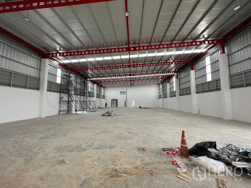 Warehouse for rent or sale in Lam Luk Ka, Pathum Thani - Spacious warehouse interior showing red steel trusses, high ceiling and metal roof panels.