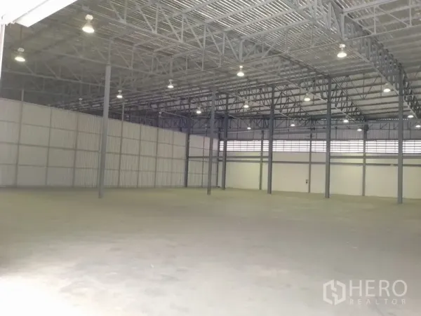Warehouse for rent in Bang Phli, Samut Prakan - Spacious warehouse interior with high-clearance steel truss roof, bright high-bay lights, and smooth concrete floor.