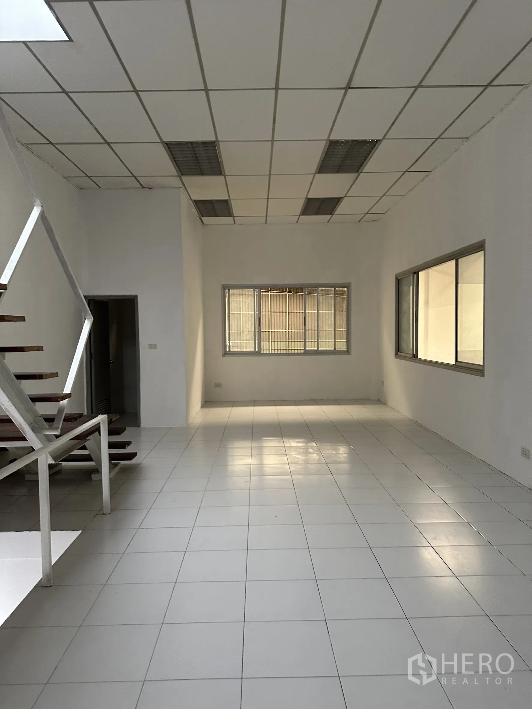 Factory for rent in Khlong Luang, Pathum Thani - Bright tiled office room with drop ceiling, windows, and staircase access.