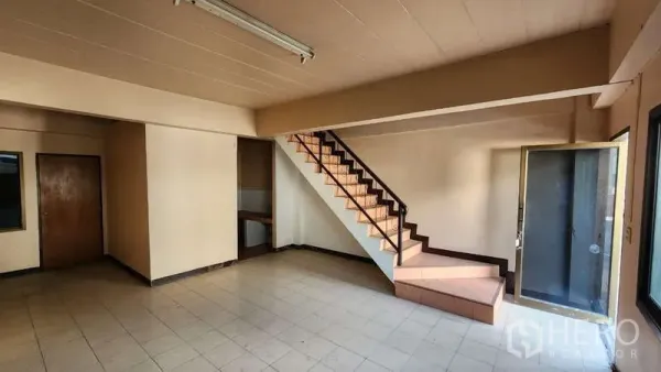 Warehouse for rent in Nong Khaem, Bangkok - Ground-floor office area with tiled flooring, staircase to upper level, and glass door entry inside the warehouse.