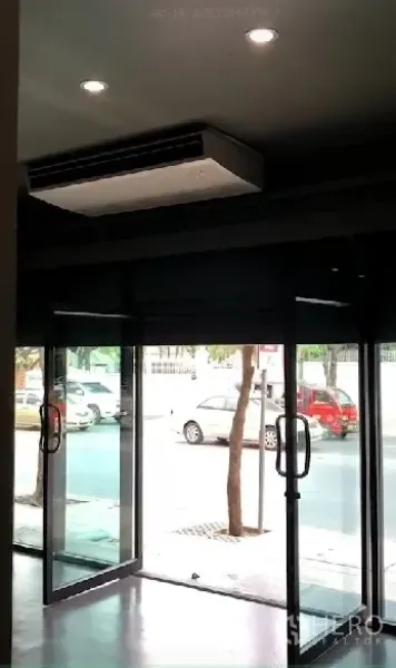 Shophouse for rent in Phra Khanong, Bangkok - Street-facing glass storefront with double doors and a ceiling cassette AC unit overlooking the sidewalk.