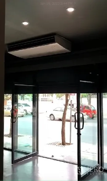 Shophouse for rent in Phra Khanong, Bangkok - Street-facing glass storefront with double doors and a ceiling cassette AC unit overlooking the sidewalk.
