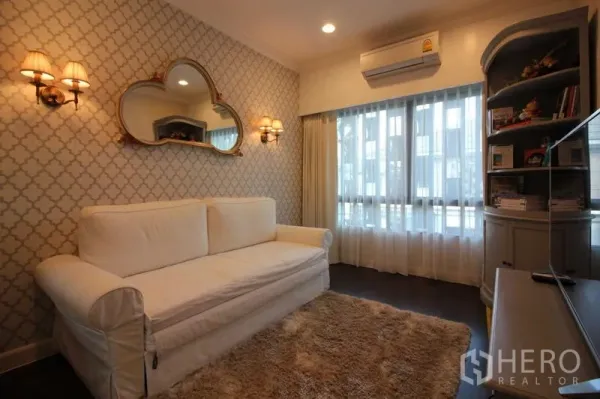 独立式住宅 出租在Prawet, Bangkok - 舒适客厅，白色沙发、几何墙纸与壁灯。