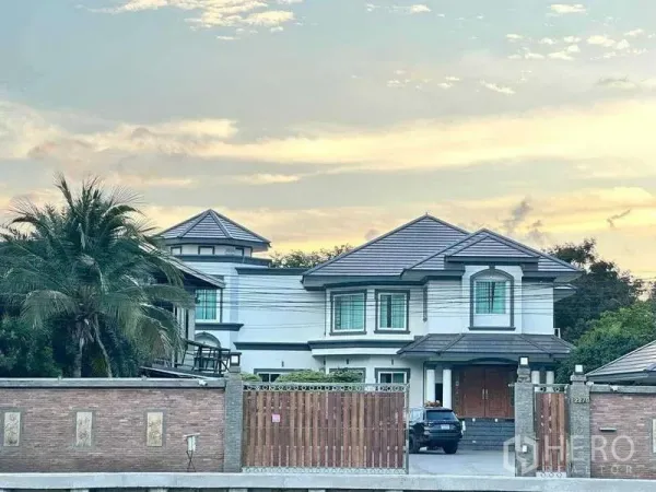 Detached House for sale in Khlong Luang, Pathum Thani - Two-storey detached house with tiled roof behind a brick wall and wooden gate at dusk in Khlong Luang.