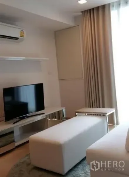 公寓 出租在Watthana, Bangkok - 明亮客厅，电视柜、白色脚凳与落地窗帘。