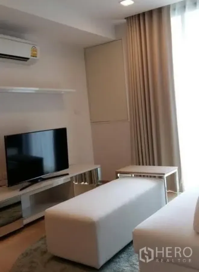 คอนโด ให้เช่าในWatthana, Bangkok - ห้องนั่งเล่นสว่างพร้อมชั้นวางทีวี ม้านั่งสีขาว และผ้าม่านเต็มความสูง