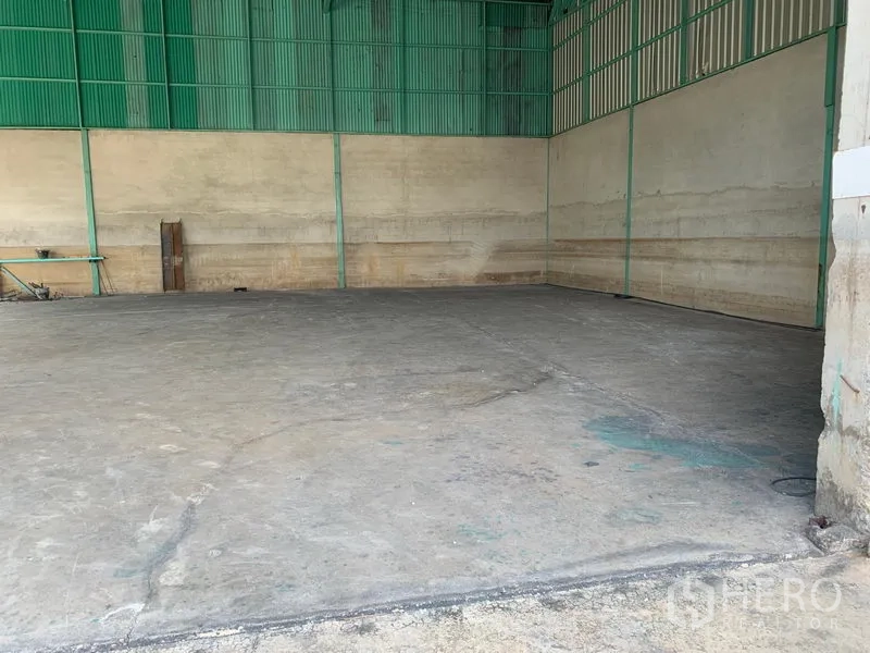 Warehouse for rent in Mueang Pathum Thani, Pathum Thani - Empty warehouse bay featuring concrete flooring and green steel wall panels.