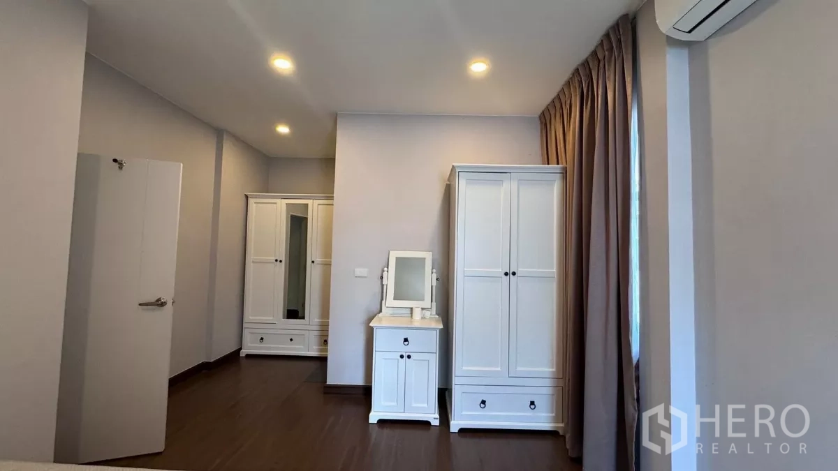 Detached House for rent or sale in Saphan Sung, Bangkok - Bedroom corner with matching white wardrobes and compact dressing table beside curtained window.