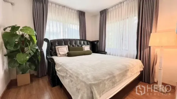 Detached House for rent or sale in Bang Khen, Bangkok - Bedroom featuring a tufted leather headboard, bedside lamp and lush greenery.