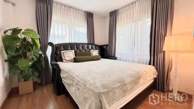 Detached House for rent or sale in Bang Khen, Bangkok - Bedroom featuring a tufted leather headboard, bedside lamp and lush greenery.