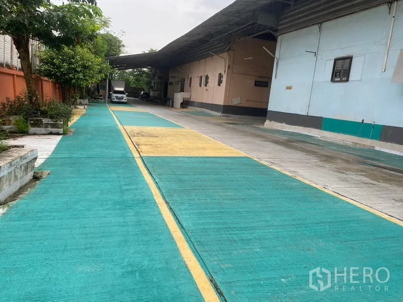 Warehouse for rent in Lam Luk Ka, Pathum Thani - Entrance lane with colored safety markings and truck-friendly canopy
