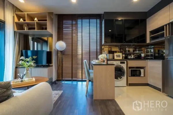 Condominium for rent or sale in Din Daeng, Bangkok - Open-plan living room and kitchenette with breakfast bar, built-in storage, TV, washing machine and tall wooden blinds in a Din Daeng condo.