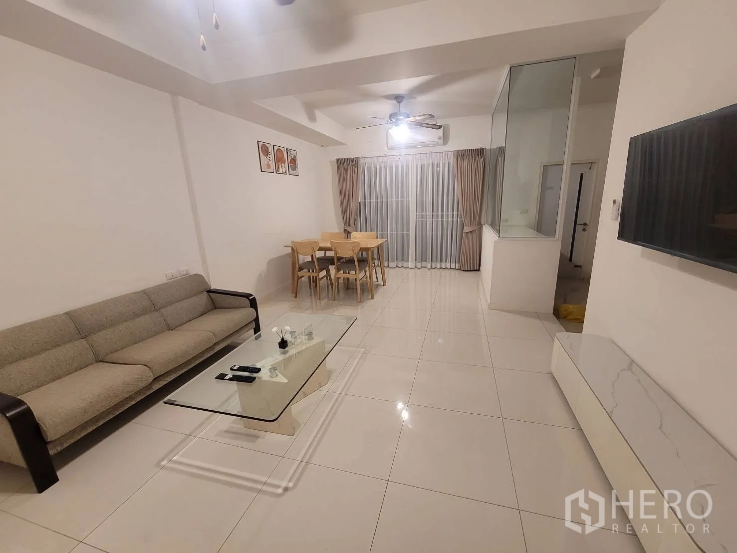 联排别墅 出租在Prawet, Bangkok - 客厅配沙发、玻璃茶几、壁挂电视与亮面地砖。