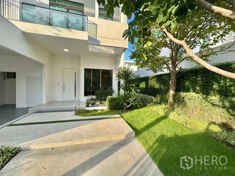 Detached House for rent in Samut Prakan - Front garden with manicured lawn, shade tree and covered entry beside the carport.