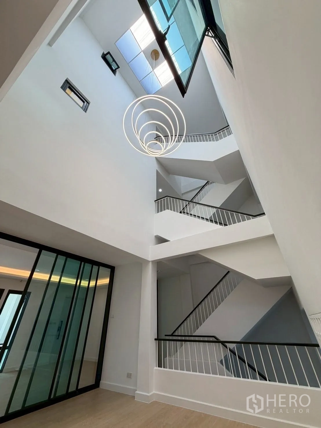 Townhouse for sale in Phra Khanong, Bangkok - Dramatic atrium with open stairs and circular pendant under a skylight.
