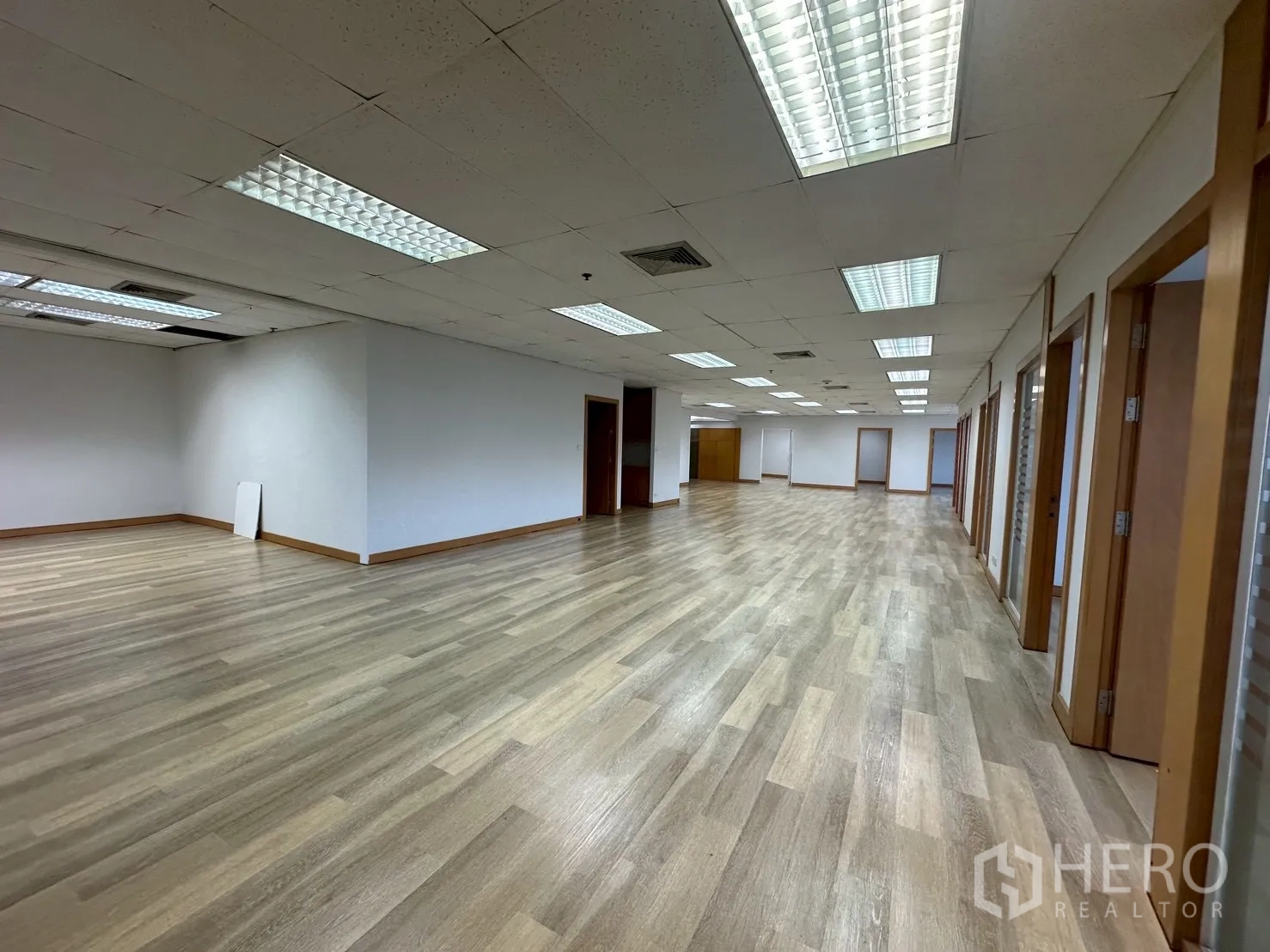Office Space for rent - Wide office area with suspended ceiling lights and partitioned rooms on both sides.