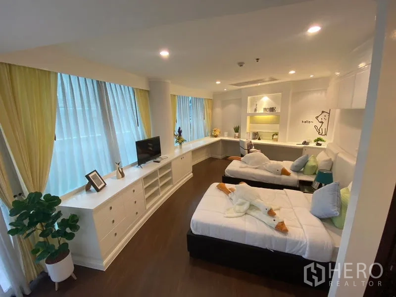 Apartment for rent in Watthana, Bangkok - Bright twin bedroom with a long built-in study desk, storage and corner windows.