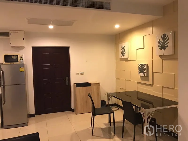 คอนโด ให้เช่าในWatthana, Bangkok - มุมรับประทานอาหารโต๊ะกระจก ผนังตกแต่งกรอบภาพ และประตูทางเข้าใต้ไฟดาวน์ไลท์