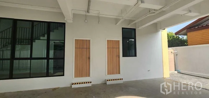 带办公室的家 出租在Bang Kapi, Bangkok - 一层带顶棚的空间，设有两扇木门、黑色框窗及外露管线。