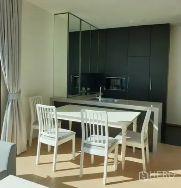 公寓 出租在Pathum Wan, Bangkok - 明亮餐区，白色餐桌椅与深色一体化橱柜及镜面背景。