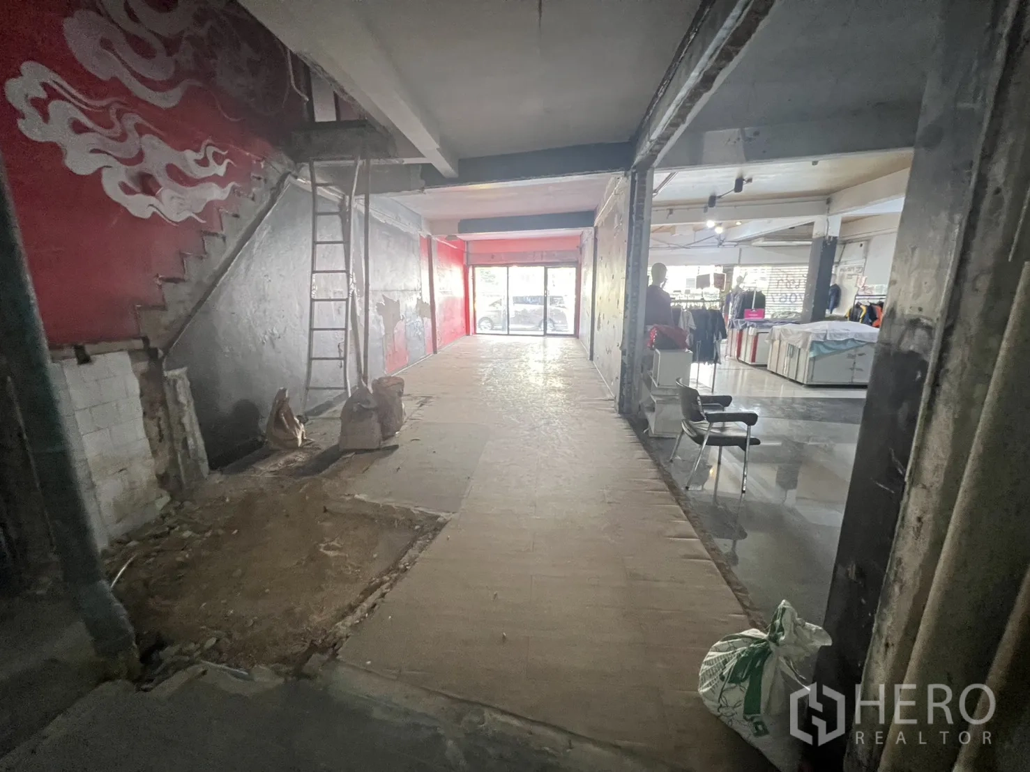 Shophouse for rent in Khlong Toei, Bangkok - Ground-floor shophouse interior with unfinished walls, concrete stairs, and a glass shopfront facing the street.