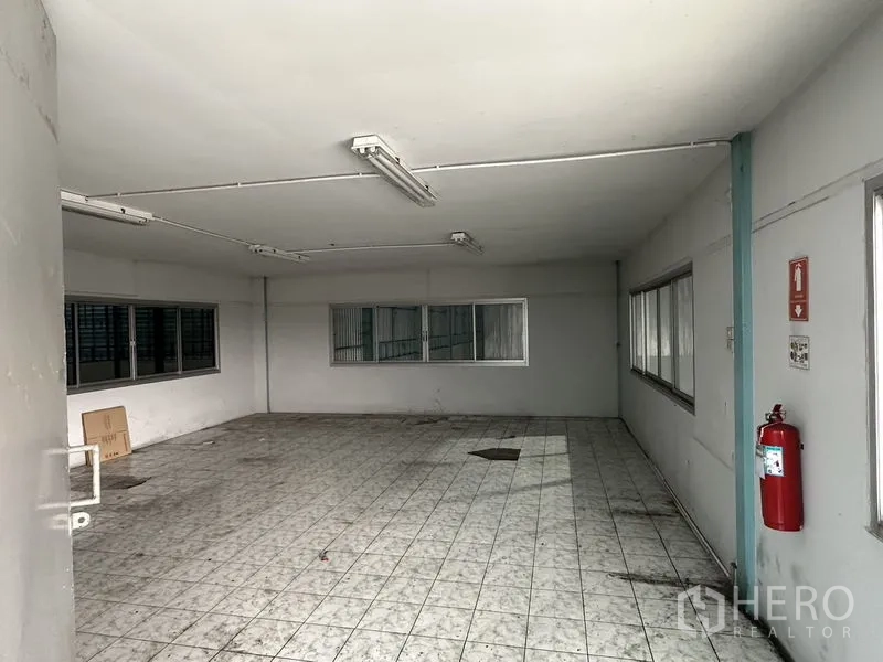 Warehouse for rent in Mueang Samut Prakan, Samut Prakan - Second-floor open office area with tiled flooring, multiple windows and a wall-mounted fire extinguisher.
