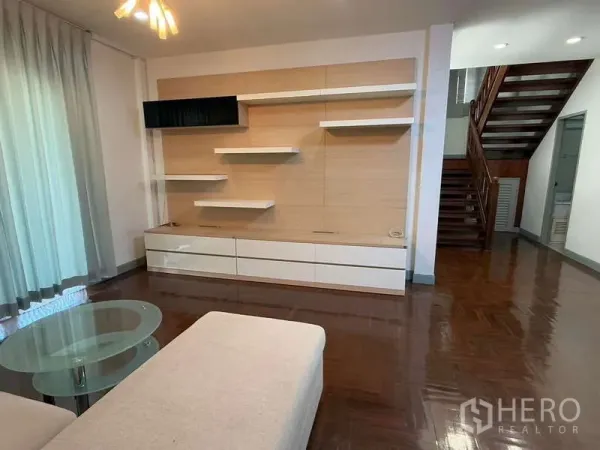 独立式住宅 出租在Bang Kapi, Bangkok - 采光良好的客厅，带内置影音墙、悬浮层板和木楼梯。