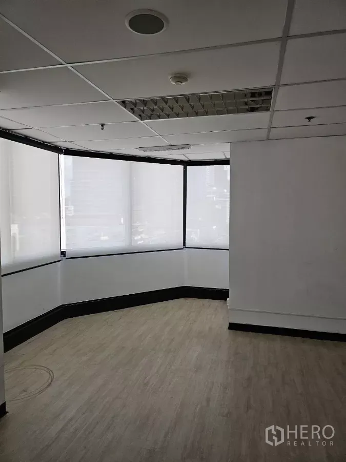 Office Space for rent in Watthana, Bangkok - Bright corner office with wrap-around windows, roller blinds, wood-look flooring, and a grid ceiling.