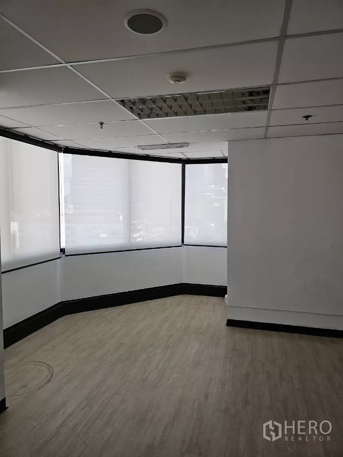 Office Space for rent in Watthana, Bangkok - Bright corner office with wrap-around windows, roller blinds, wood-look flooring, and a grid ceiling.
